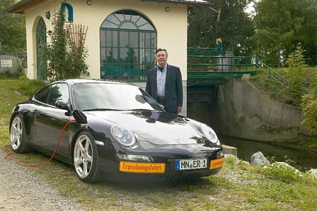 Alois Ruf mit seinem E-Ruf Porsche stilecht vor einem Wasserkraftwerk